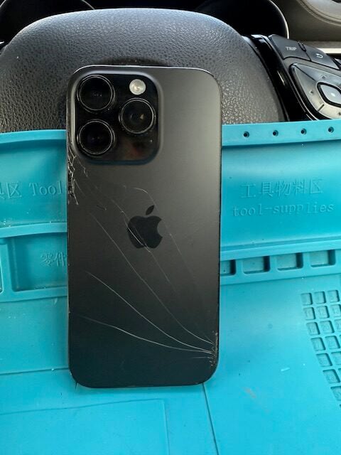 iPhone 16 Pro with cracked back glass before repair on blue workstation mat