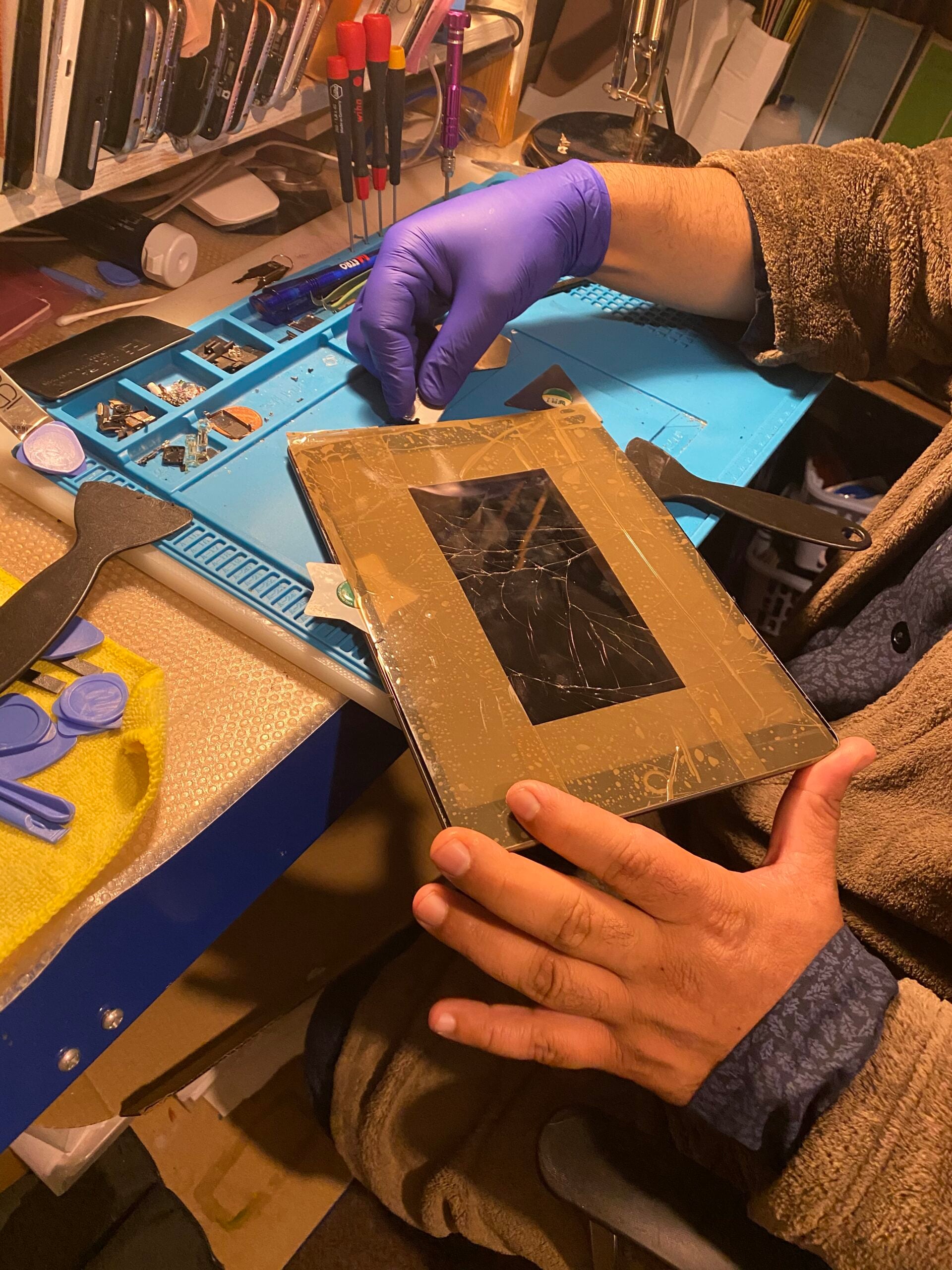 Gloved iRepairMan technician carefully repairing a cracked iPad screen on a professional repair mat.