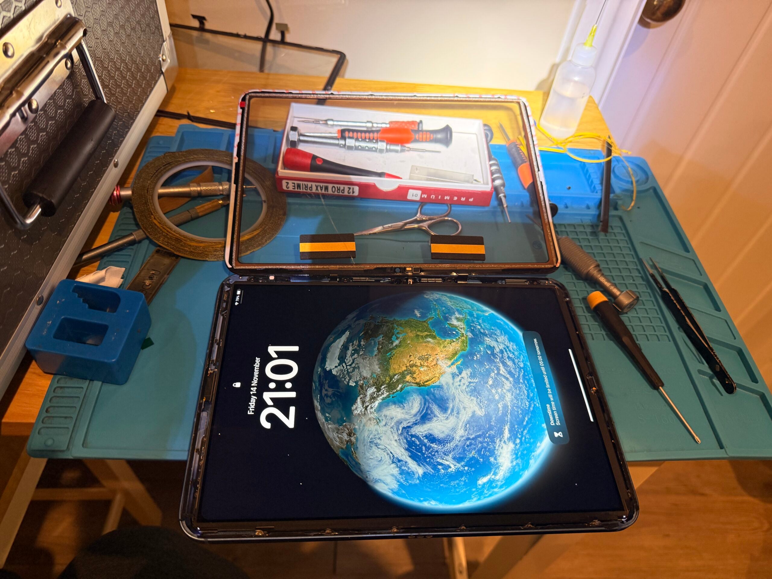 iPad screen replacement in progress with the display assembly lifted and tools on a blue repair mat.