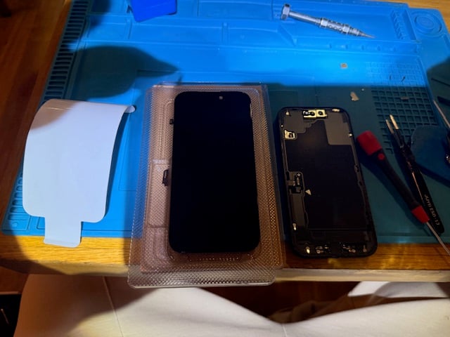 iPhone 16 disassembled on repair mat during screen replacement at Heathrow Terminal 3