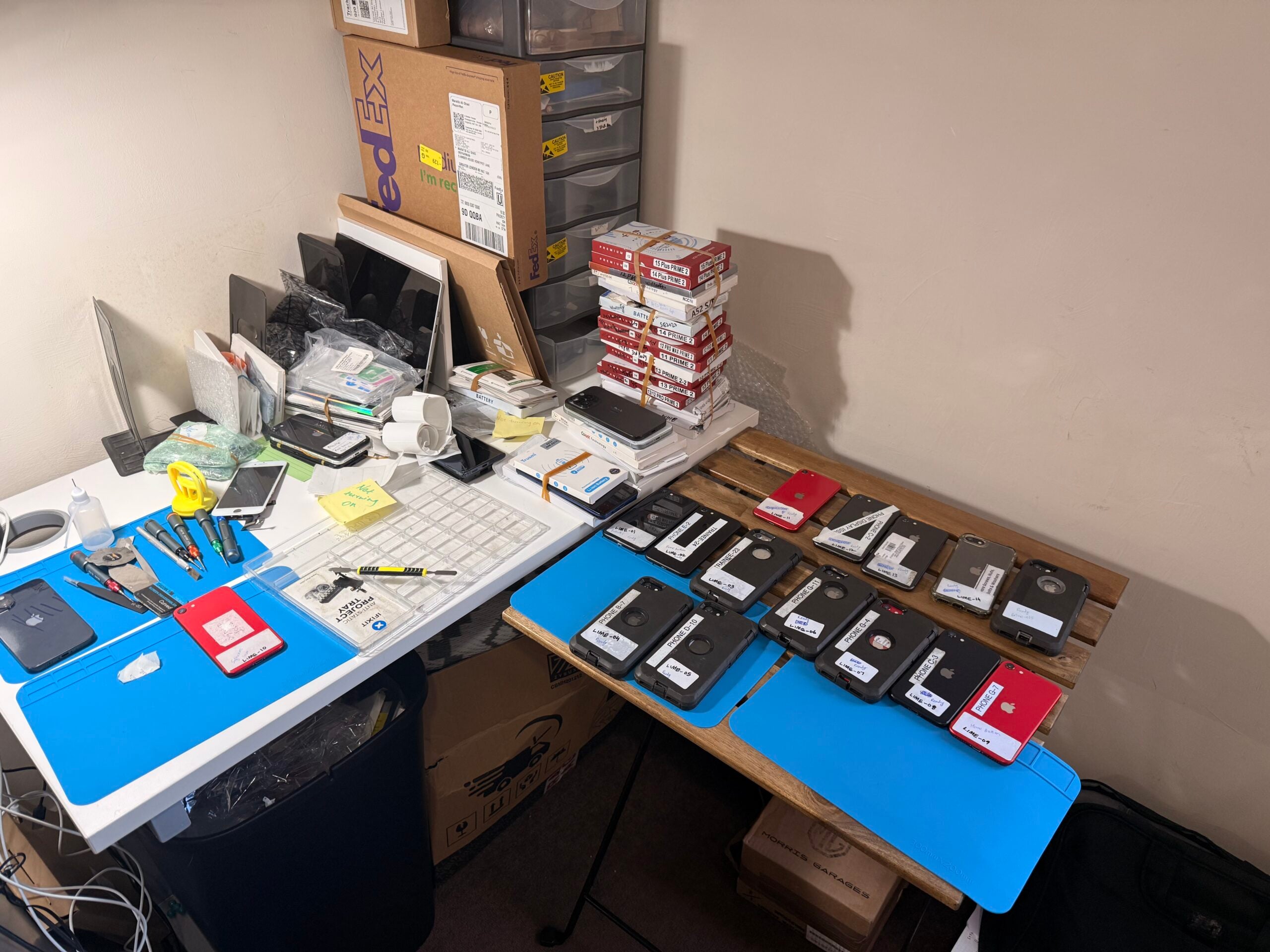 Busy iRepairMan repair workstation with multiple smartphones, parts and packaging ready for repair.