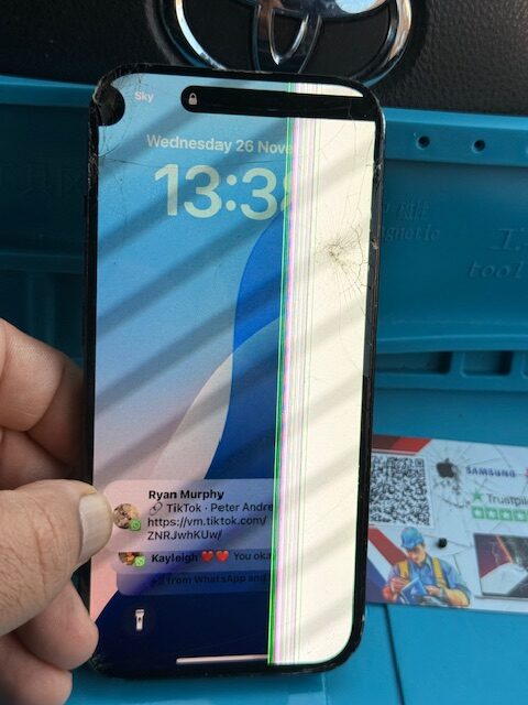 iPhone 15 screen before repair showing cracked display and damage on a Hackney construction site
