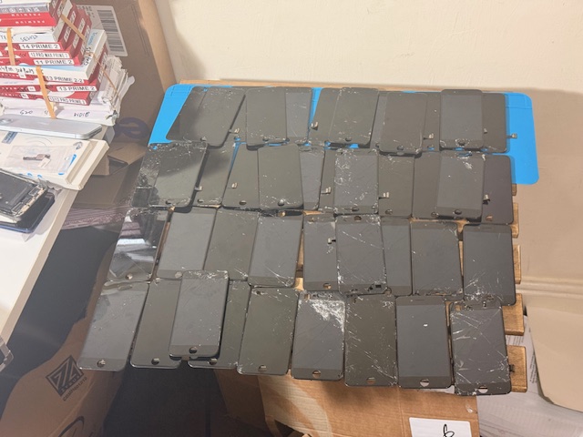 Before: multiple iPhones with broken and cracked screens ready for repair at a Barnet workplace