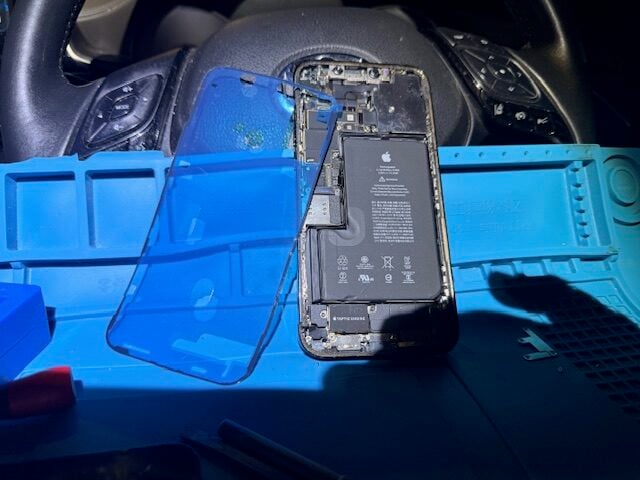 iPhone 12 Pro Max mid-repair stage with parts aligned for screen replacement