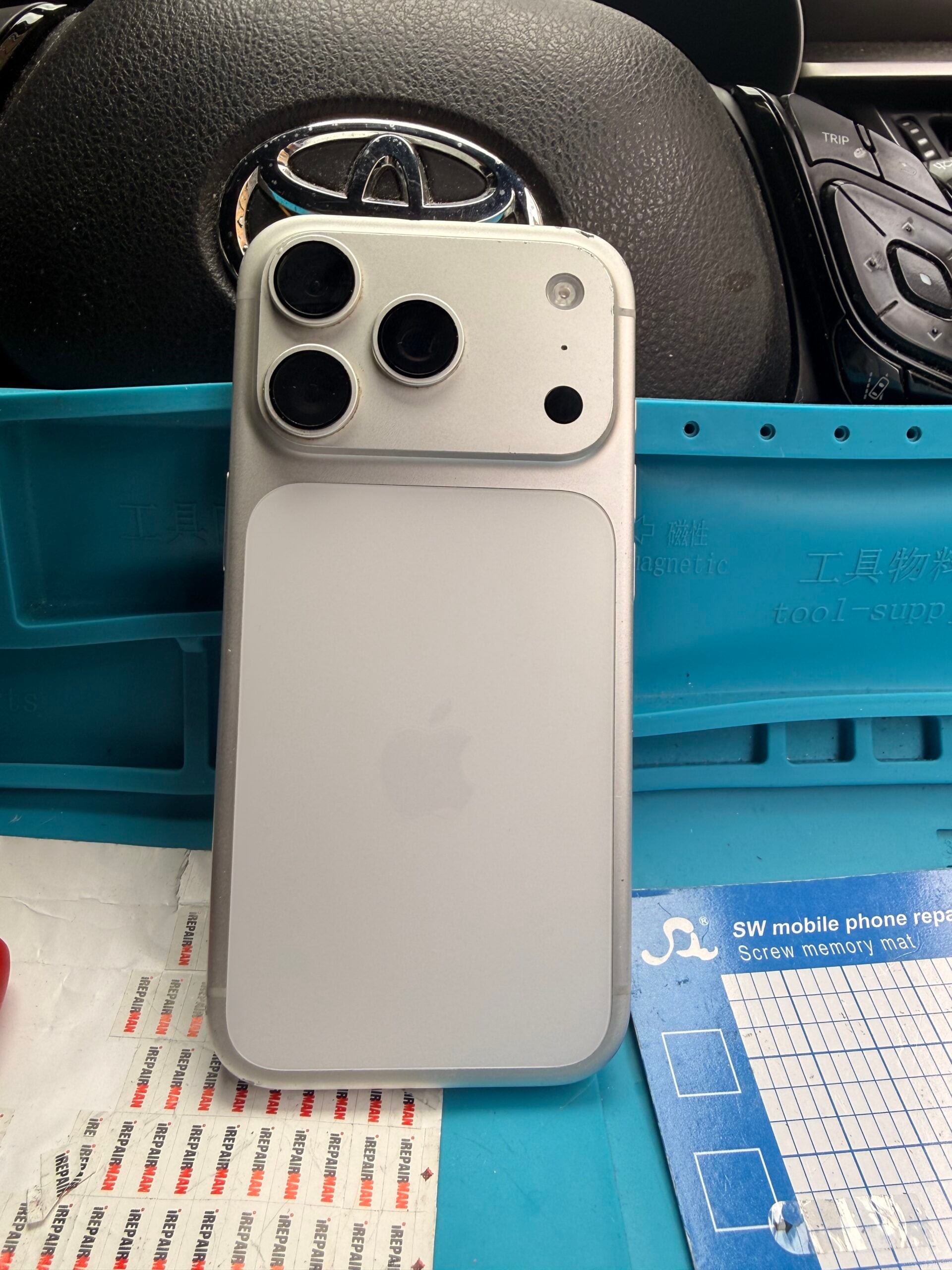 Rear view of a silver iPhone 17 Pro showing its three camera lenses on a turquoise repair mat.
