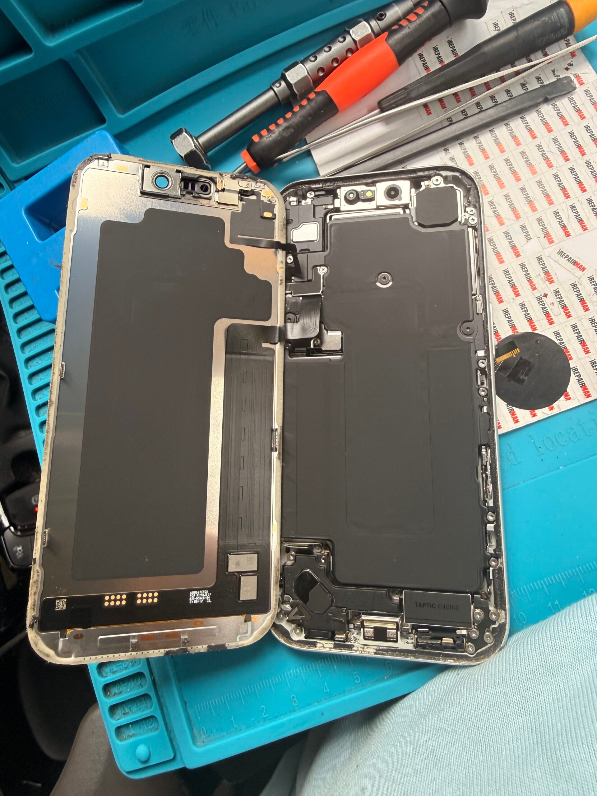 Open iPhone 17 Pro with its display lifted to the left, exposing internal covers and ribbon cables beside repair tools.