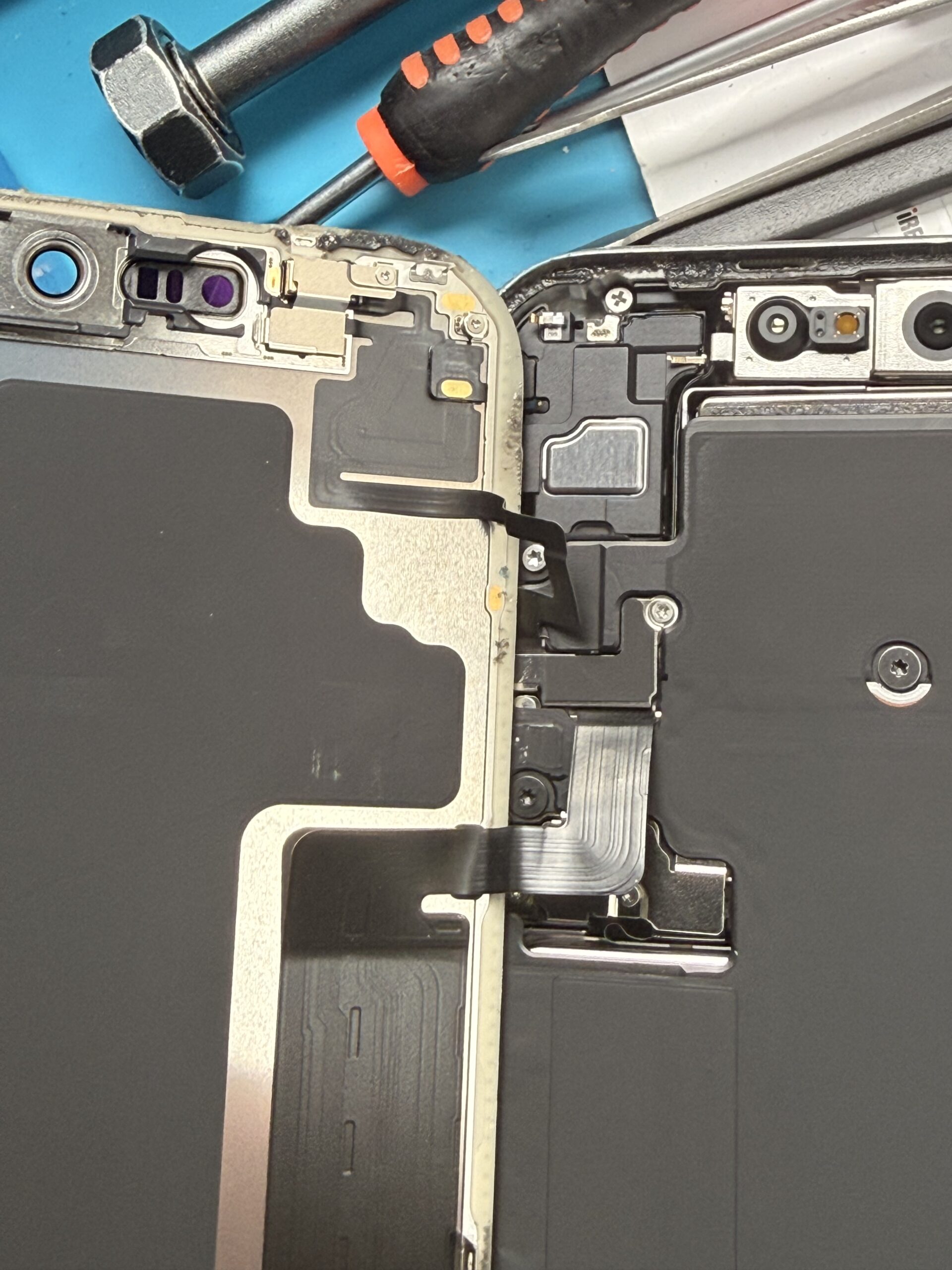 Close-up of ribbon cables connecting the lifted iPhone display to the handset, with screws and internal covers visible.