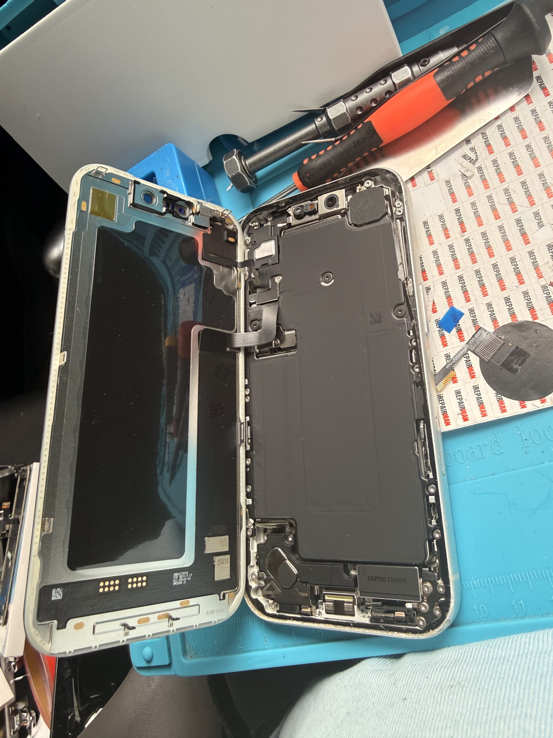Angled view of an opened iPhone 17 Pro with the display beside the body and precision tools arranged above it.