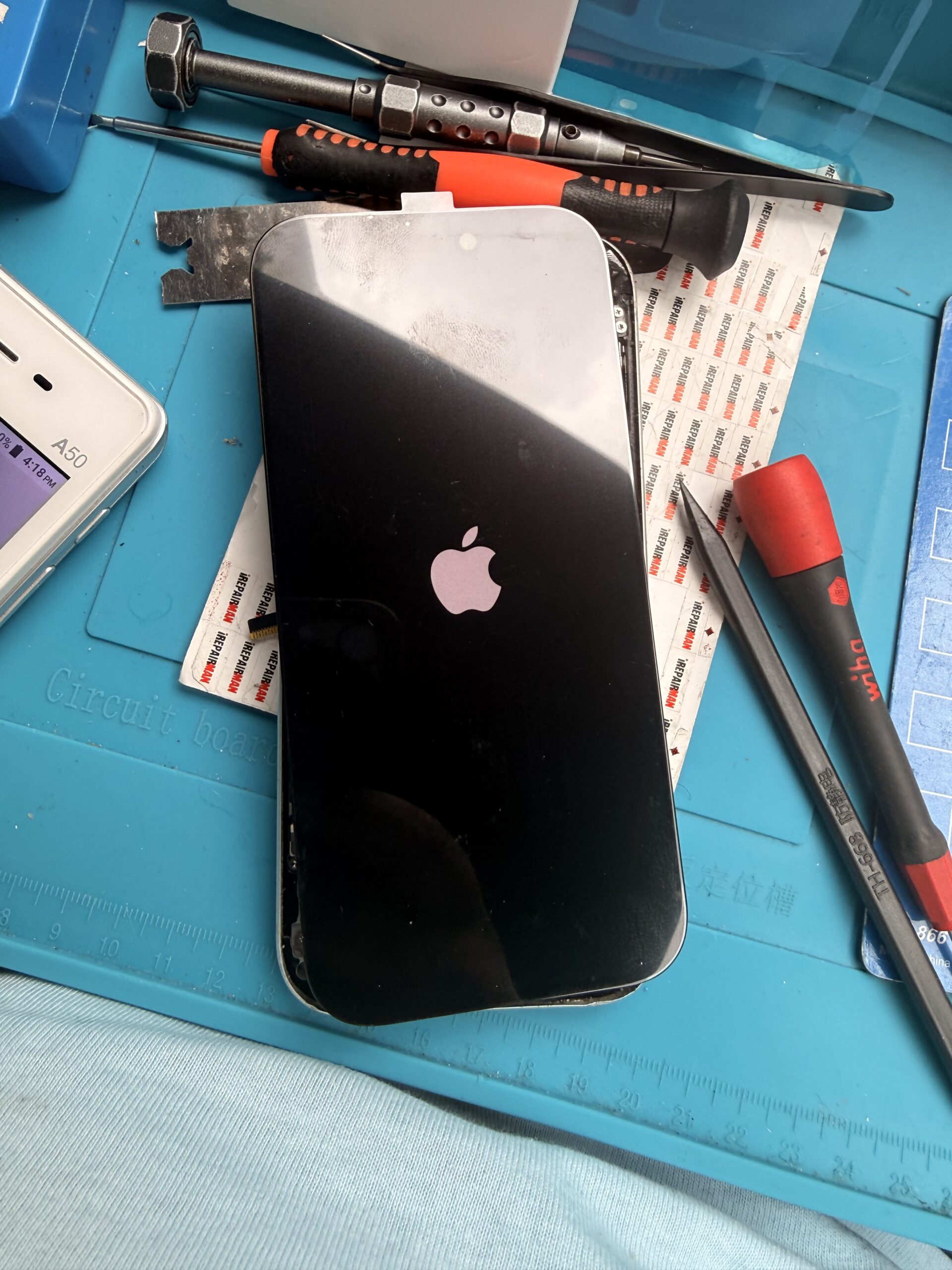Replacement iPhone 17 Pro display showing the Apple startup logo while resting over the handset on a repair mat.