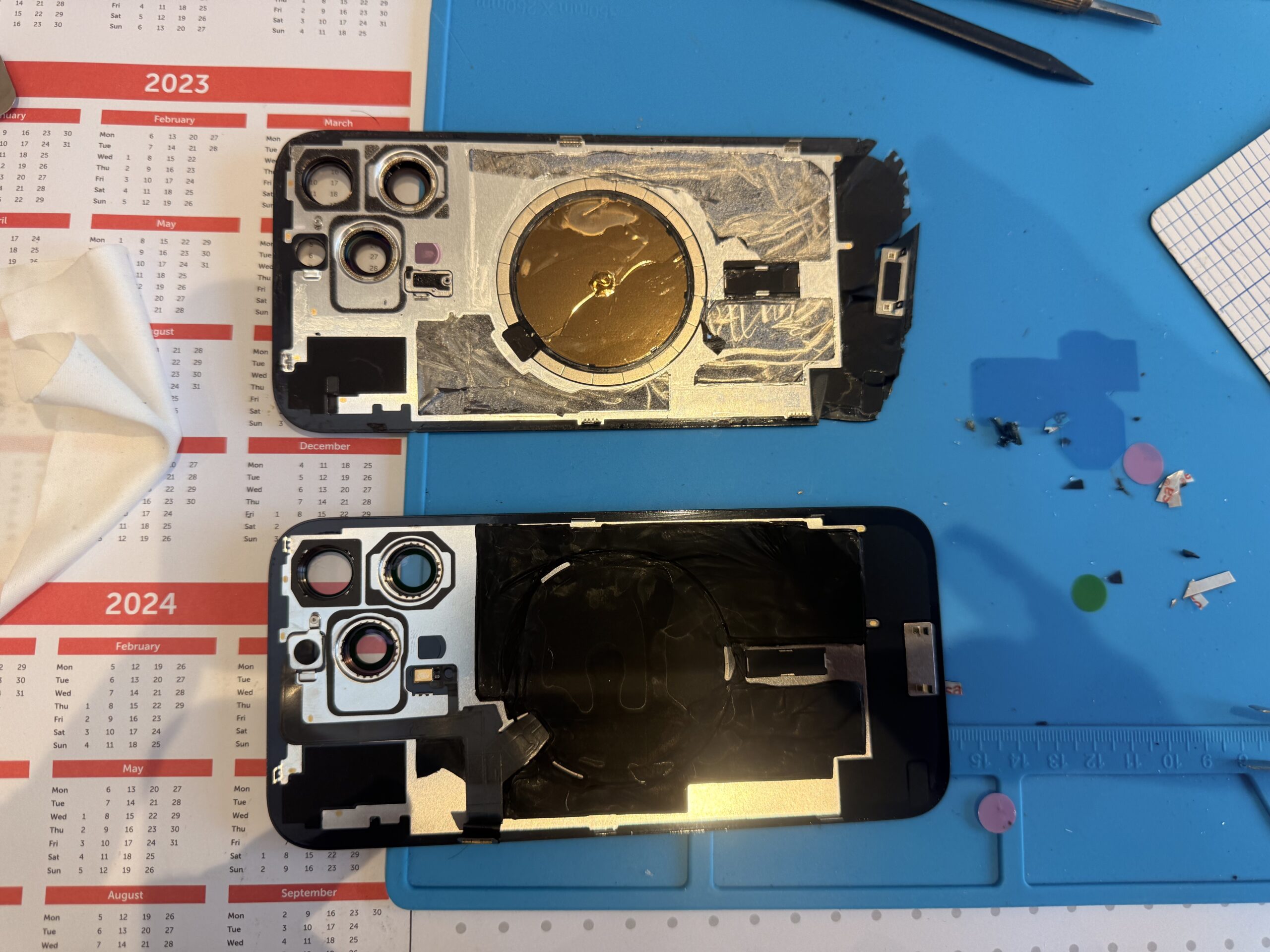 The inner faces of two iPhone 16 Pro Max back panels lie on a blue repair mat, showing camera openings and circular assembly areas.